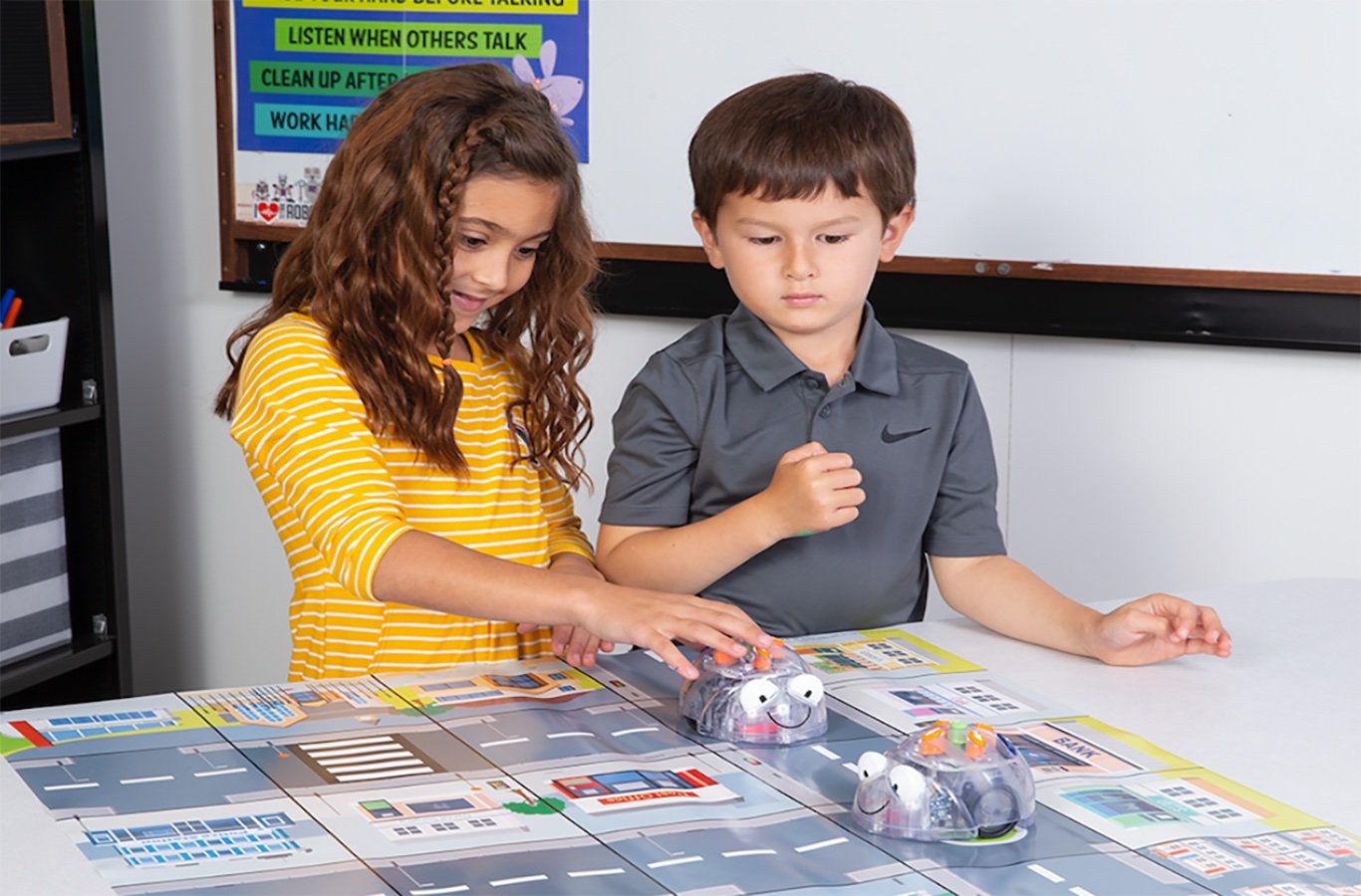 A boy and girl student playing with a Blue-Bot.